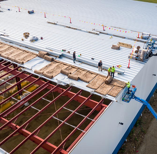 MILWAUKEE, WI, USA - SEPTEMBER 15, 2020: Construction workers installing insulation and roof panels on a large warehouse building.